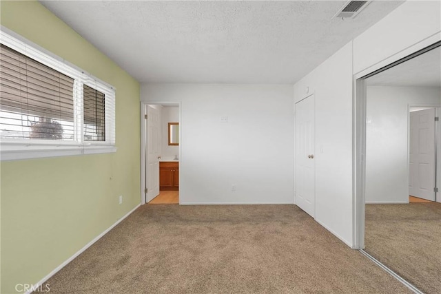 unfurnished bedroom featuring a closet, connected bathroom, light carpet, and a textured ceiling