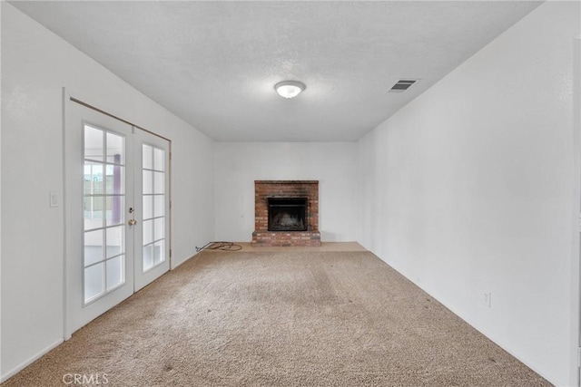 unfurnished living room with a brick fireplace, carpet flooring, and french doors