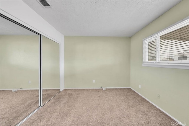 unfurnished bedroom featuring light colored carpet, a textured ceiling, and a closet