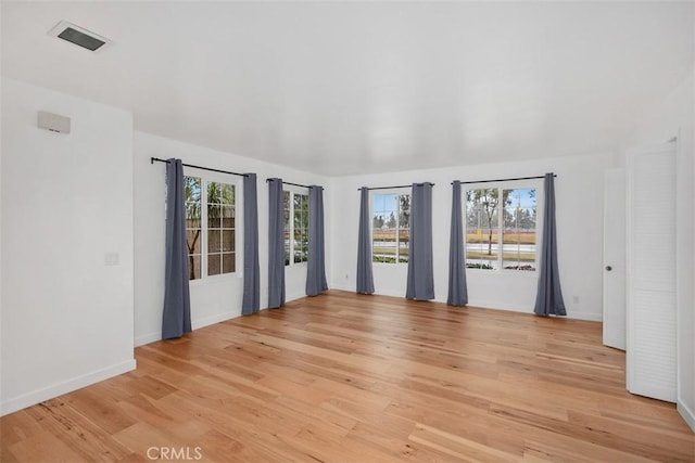 empty room featuring light wood-style floors, baseboards, and visible vents