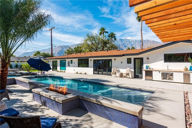 view of swimming pool with a patio area, area for grilling, a hot tub, a mountain view, and a fire pit