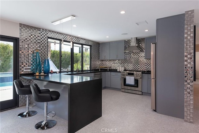 kitchen with decorative light fixtures, backsplash, high end stainless steel range, kitchen peninsula, and wall chimney range hood