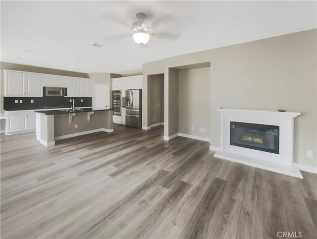 kitchen with a breakfast bar, wood-type flooring, a center island with sink, appliances with stainless steel finishes, and white cabinets