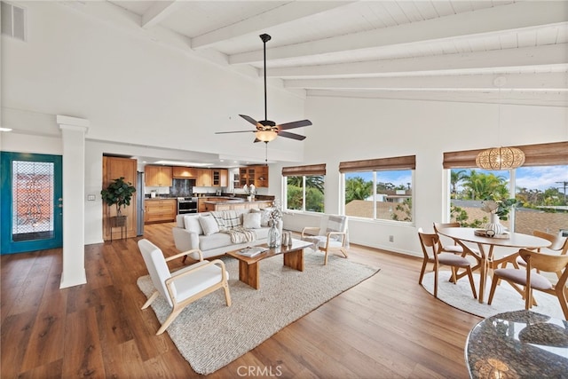 living room with ornate columns, wood-type flooring, high vaulted ceiling, beamed ceiling, and ceiling fan