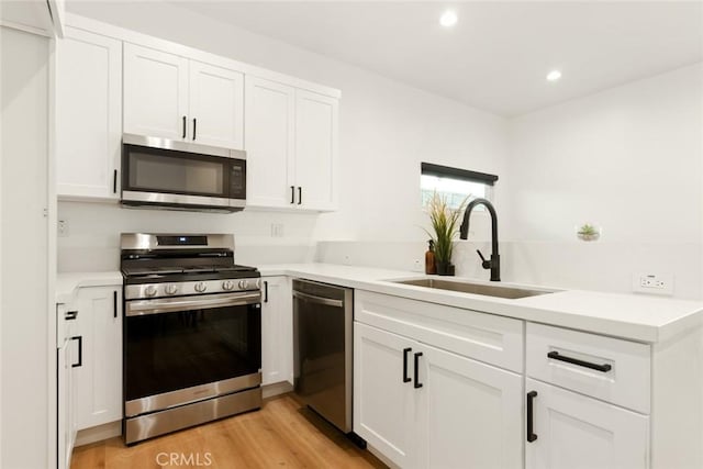 kitchen featuring stainless steel appliances, a sink, white cabinets, light countertops, and light wood finished floors