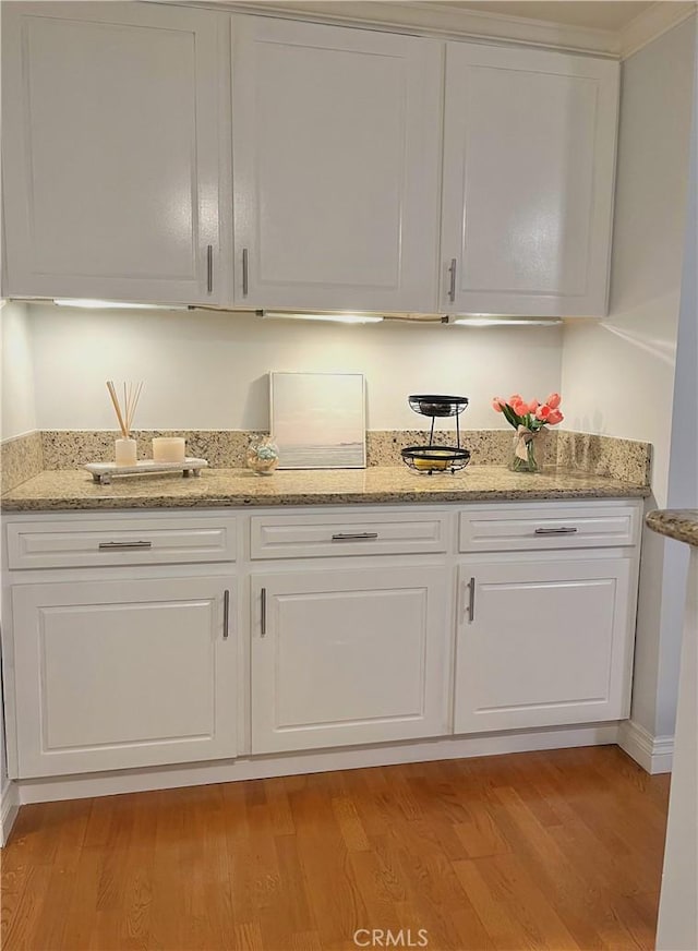 bar featuring light hardwood / wood-style floors, white cabinetry, and light stone counters