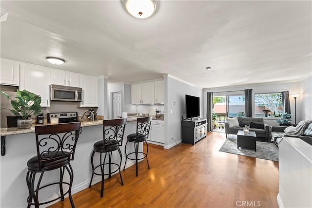 kitchen with a breakfast bar, light hardwood / wood-style flooring, light stone countertops, appliances with stainless steel finishes, and white cabinets