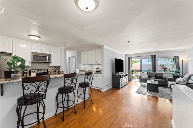 kitchen with appliances with stainless steel finishes, light stone counters, light hardwood / wood-style floors, a breakfast bar, and white cabinetry