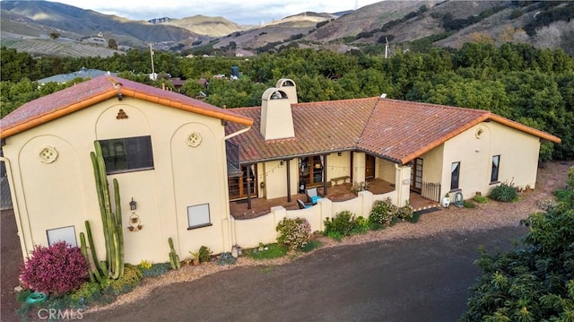 mediterranean / spanish house featuring a tile roof, a chimney, a mountain view, and stucco siding