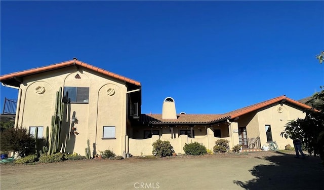 rear view of house with a tiled roof, a chimney, and stucco siding