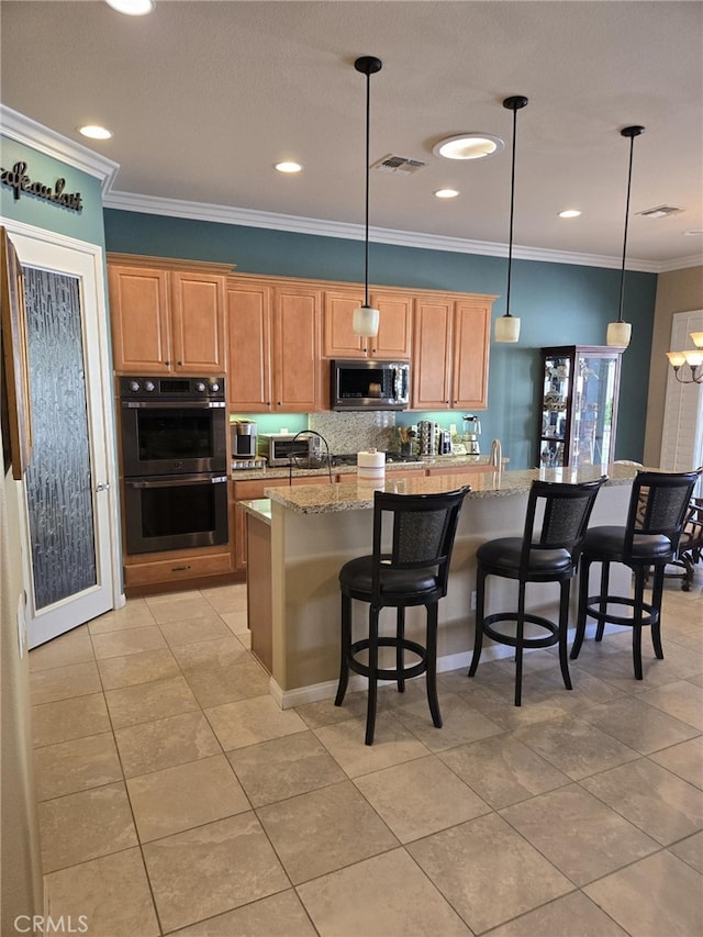 kitchen featuring appliances with stainless steel finishes, decorative light fixtures, an island with sink, a kitchen bar, and light stone counters