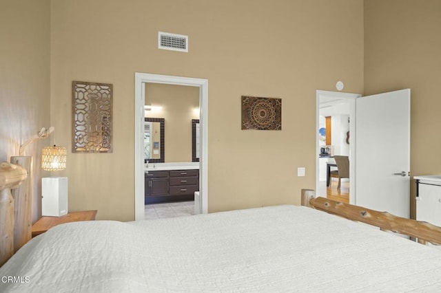 bedroom with ensuite bathroom, a towering ceiling, and light tile patterned floors