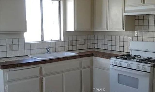 kitchen featuring a sink, gas range gas stove, backsplash, and white cabinetry
