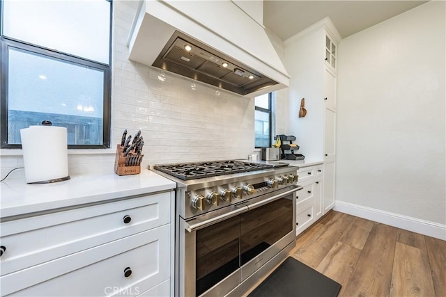 kitchen featuring light hardwood / wood-style flooring, premium range hood, white cabinetry, decorative backsplash, and range with two ovens