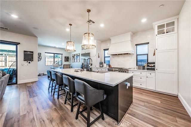 kitchen with hanging light fixtures, premium range hood, white cabinets, and a center island with sink