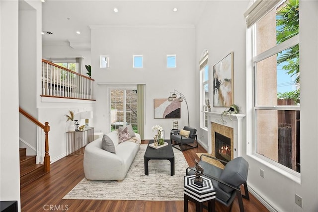 living room featuring a fireplace with flush hearth, wood finished floors, crown molding, baseboards, and stairs