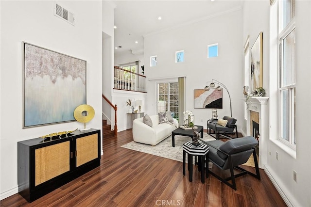 living area with stairs, a towering ceiling, a fireplace, ornamental molding, and visible vents