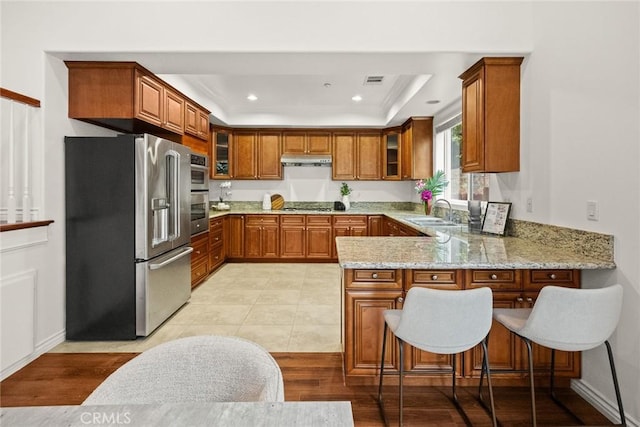 kitchen with a peninsula, brown cabinetry, appliances with stainless steel finishes, and under cabinet range hood
