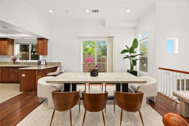 dining room featuring wood finished floors, visible vents, ornamental molding, and a healthy amount of sunlight
