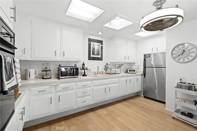 kitchen with light wood-type flooring, a skylight, stainless steel refrigerator, sink, and white cabinetry