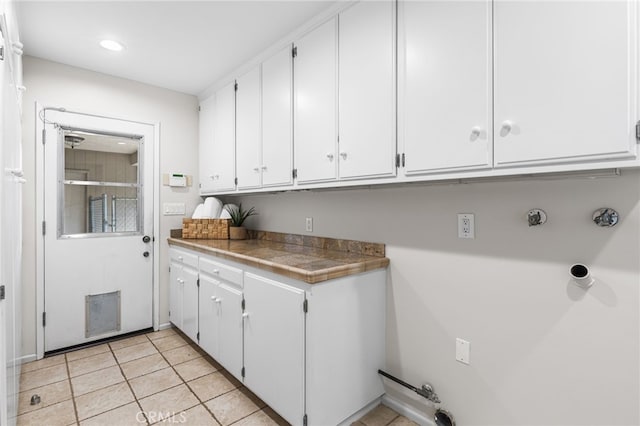 clothes washing area with cabinets and light tile patterned floors