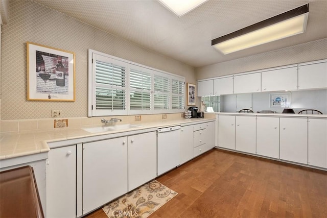 kitchen featuring sink, white cabinetry, tile countertops, white dishwasher, and hardwood / wood-style floors