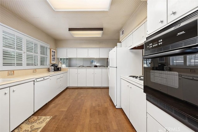 kitchen with white cabinetry, black oven, dishwasher, and light hardwood / wood-style flooring