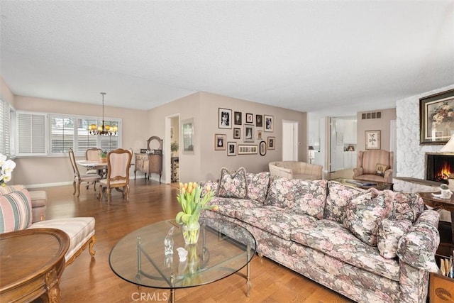 living room with a fireplace, a chandelier, a textured ceiling, and light wood-type flooring