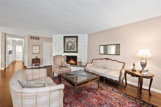 living room with hardwood / wood-style flooring, a stone fireplace, and a textured ceiling