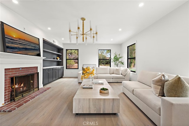 living area featuring recessed lighting, light wood-style floors, a brick fireplace, and a chandelier