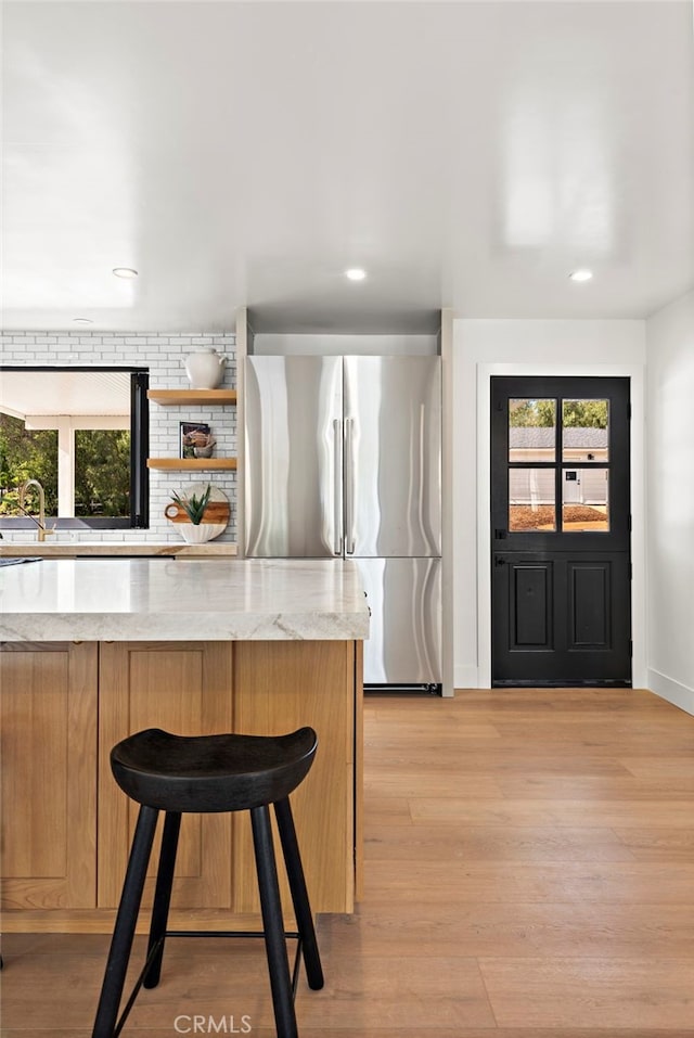 kitchen featuring a kitchen bar, a sink, tasteful backsplash, freestanding refrigerator, and light wood finished floors