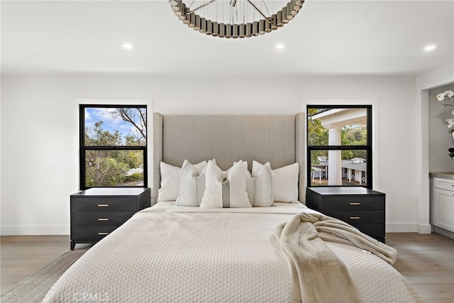 bedroom with light wood-type flooring, baseboards, and an inviting chandelier