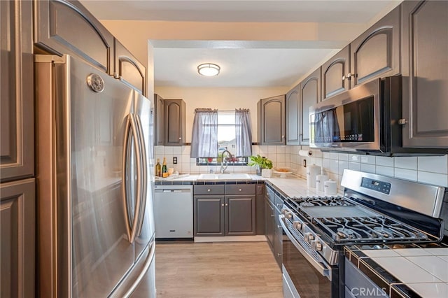 kitchen featuring appliances with stainless steel finishes, sink, decorative backsplash, tile counters, and light wood-type flooring