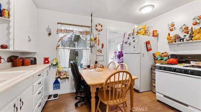 kitchen with sink, white appliances, wood-type flooring, and white cabinets