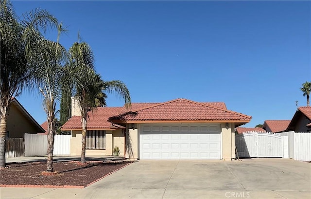 mediterranean / spanish house featuring a garage, a gate, a tiled roof, and stucco siding