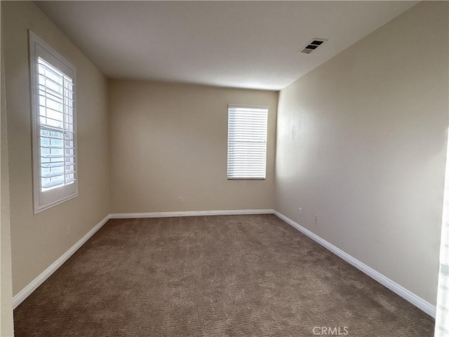 unfurnished room featuring baseboards, visible vents, and dark colored carpet