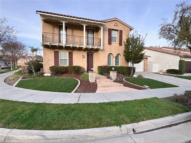 mediterranean / spanish house featuring a balcony, a garage, driveway, stucco siding, and a front yard