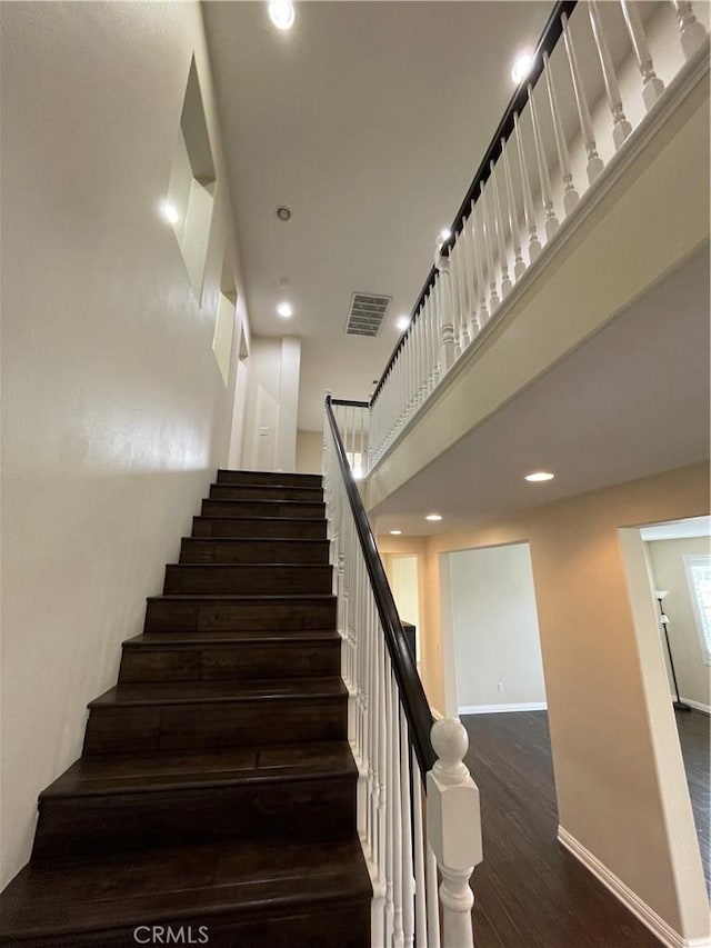 staircase with recessed lighting, visible vents, a towering ceiling, wood finished floors, and baseboards