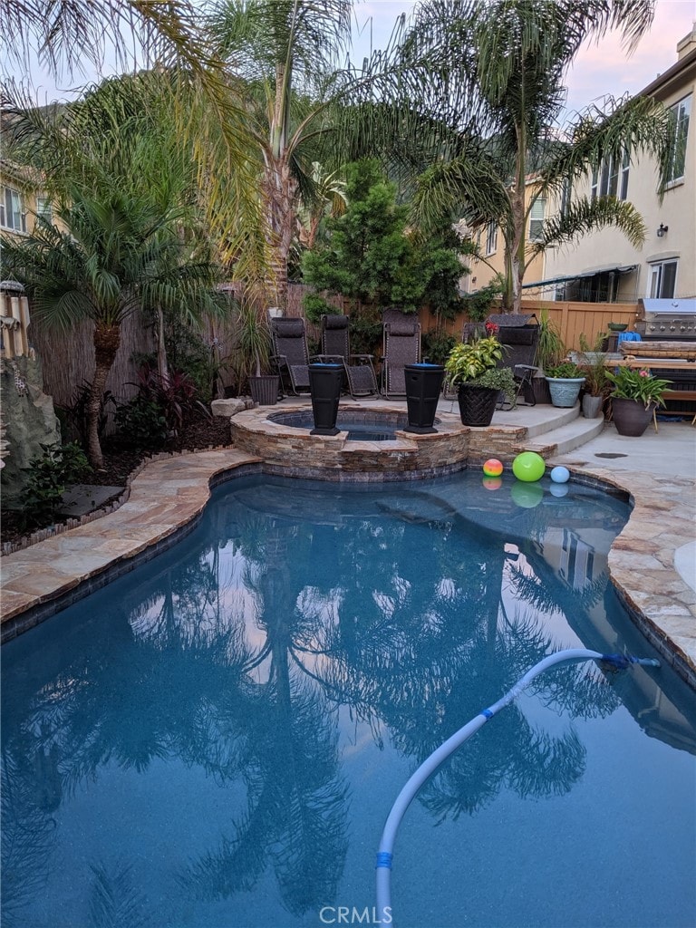 pool at dusk featuring a patio area and an in ground hot tub