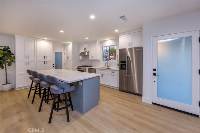 kitchen with light stone counters, stainless steel appliances, a center island, and white cabinets