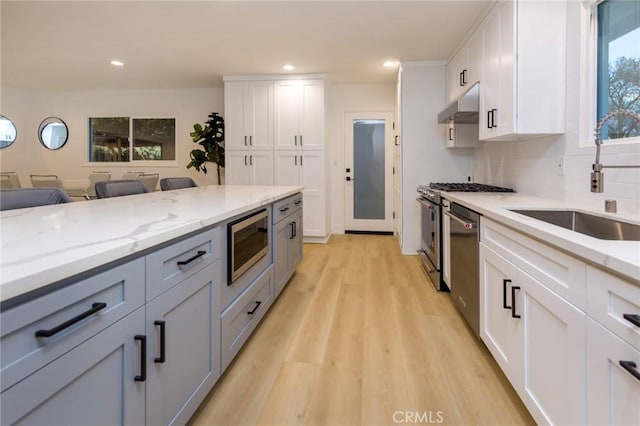 kitchen with sink, white cabinetry, light stone counters, light hardwood / wood-style flooring, and appliances with stainless steel finishes