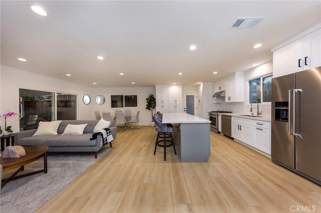 kitchen with sink, a breakfast bar, white cabinetry, stainless steel appliances, and a center island