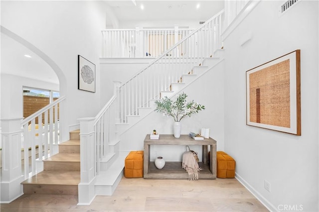 stairs with baseboards, visible vents, arched walkways, a towering ceiling, and wood finished floors