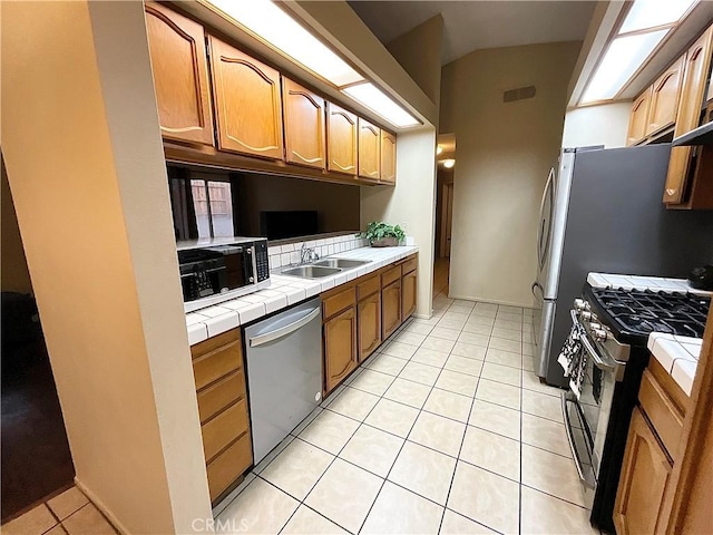 kitchen with stainless steel appliances, tile counters, sink, and light tile patterned floors