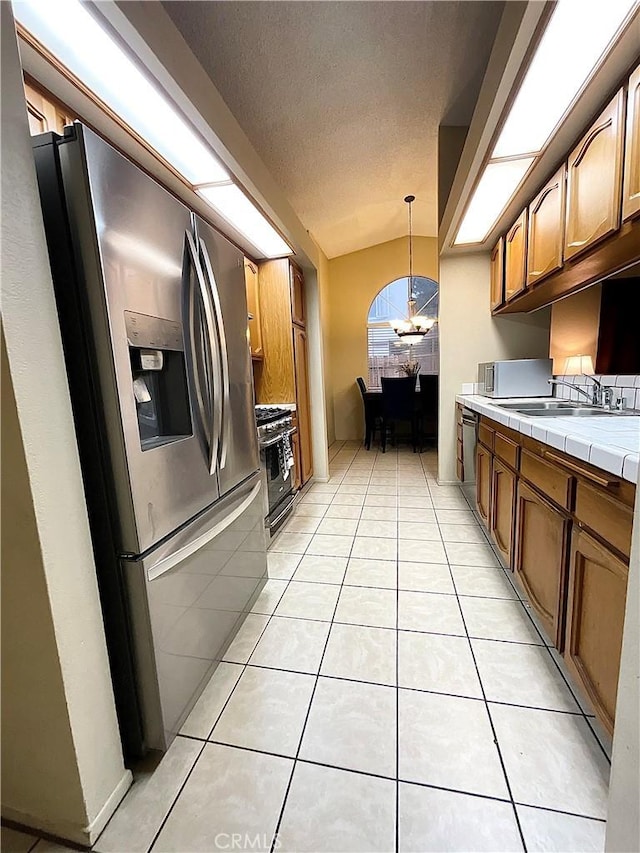 kitchen with appliances with stainless steel finishes, tile countertops, sink, hanging light fixtures, and light tile patterned floors