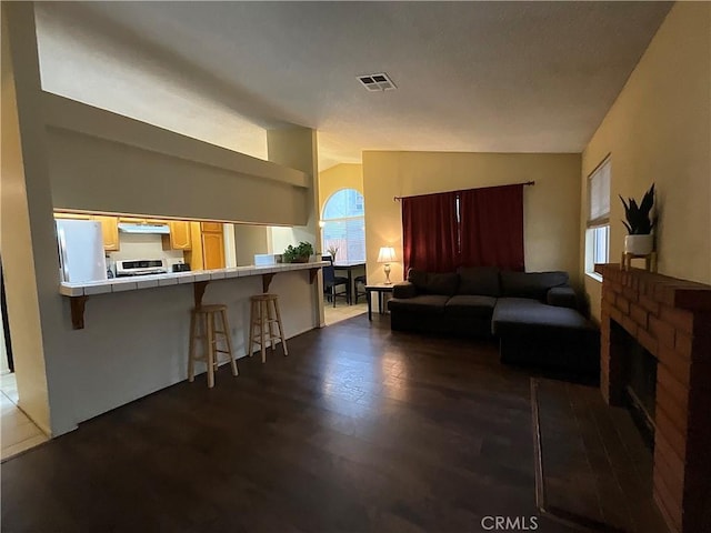 living room featuring lofted ceiling, dark hardwood / wood-style flooring, and a brick fireplace