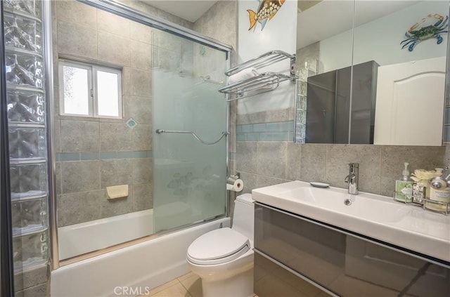 full bathroom with tile walls, bath / shower combo with glass door, vanity, decorative backsplash, and toilet