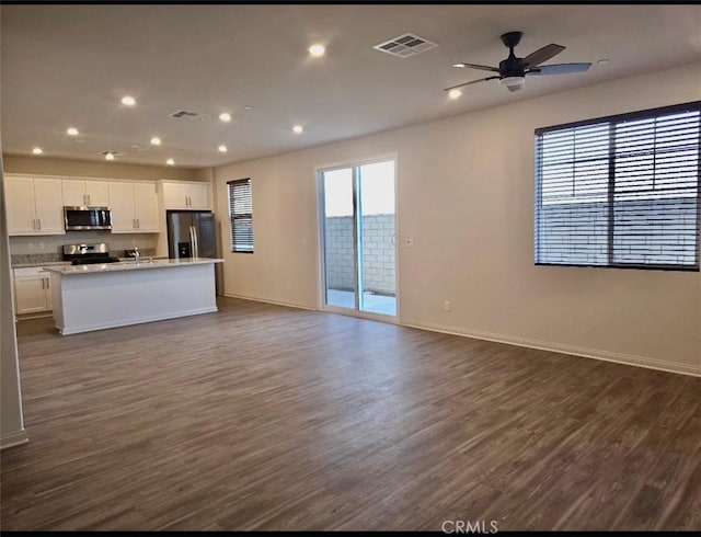 kitchen with appliances with stainless steel finishes, dark hardwood / wood-style flooring, an island with sink, and white cabinets