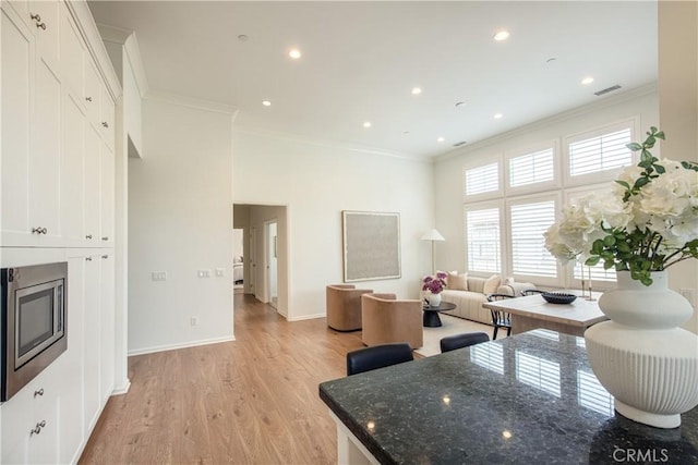 living room with a large fireplace, a towering ceiling, crown molding, and light hardwood / wood-style flooring