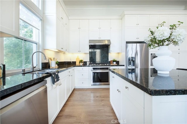 kitchen with light wood-type flooring, dark stone countertops, sink, appliances with stainless steel finishes, and white cabinets